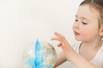 A girl is exploring the planet earth. A child is playing with a globe. Little girl is looking for her country on the globe