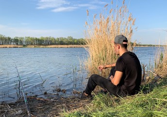 Concept: hobby, fishing, nature, recreation. Guy is sitting on the Bank of the river with a fishing rod during the day.