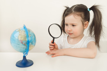 A girl is exploring the planet earth. A child is playing with a globe. Little girl is looking for...