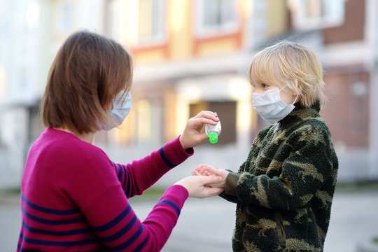 Young Woman And Little Child Wearing A Protective Mask Makes Disinfection Of Hands With Sanitizer In Airport, Supermarket Or Other Public Place. Safety During COVID-19 Outbreak.