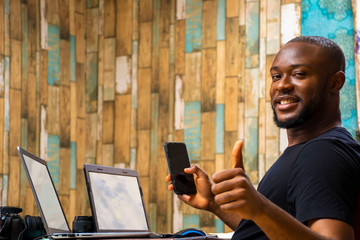 young black man working on his laptop in his office and pressing his phone