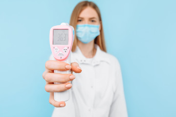 A female doctor in a protective mask measures the temperature using a non-contact infrared thermometer