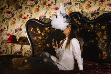 woman smokes a e-cigarette lying on the bed in the room. Smoker's concept Vaping.