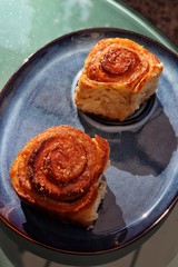 Homemade cinnamon rolls, freshly baked, on a blue plate and azure glass table. Closeup and top view.