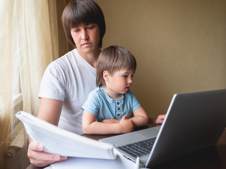 Self-isolation because of coronavirus outbreak. Man is remote working with his little son. Laptop on table.