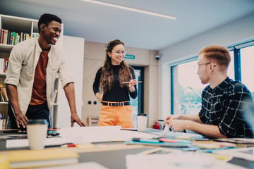 Cheerful millennial men and woman laughing during break from learning in coworking space discussing funny ideas for university project, happy hipsters teambuilding during developing design homework