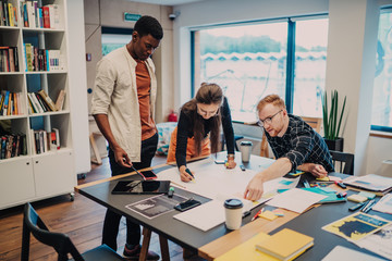 Millennial group of divers developers creating architect project using blueprint sketch at table...