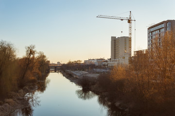 Cityscape with river.Construction of multi-storey residential building over the river is illuminated by the sunset. 