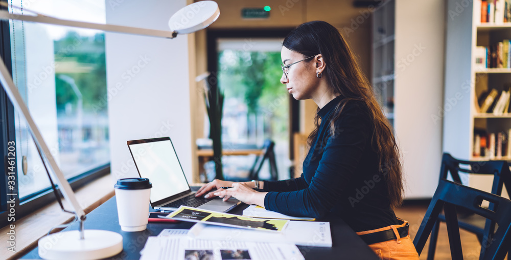 Poster side view of millennial graphic designer working remotely with web project on modern blank laptop wi