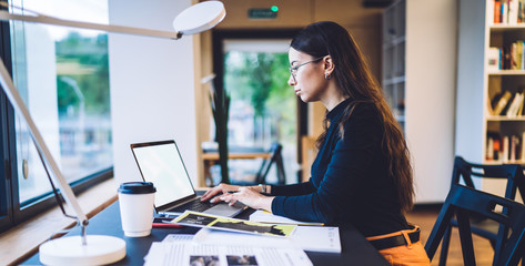 Side view of millennial graphic designer working remotely with web project on modern blank laptop...