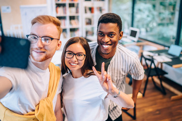 Cheerful coworkers gesturing and taking selfie in office