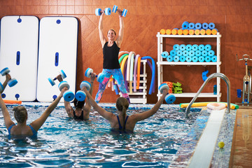 Young girls and middle-aged women do aqua aerobics with dumbbells in a swimming pool with a trainer, fitness exercises for weight loss in water
