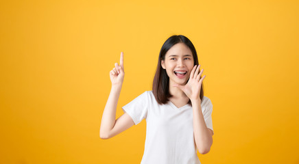 Attractive young asian woman announcing with hands to the mouth  and telling a secret, isolated on light orange background