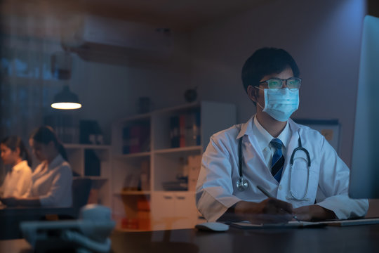 The Doctor Wearing Mask Is Sitting At A Desk At The Night, Which Is Researching How To Treat The Patient's Condition.