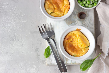 Green peas and cheese souffle in a white ceramic ramekin on light wooden board. Classic french meal. Top view.