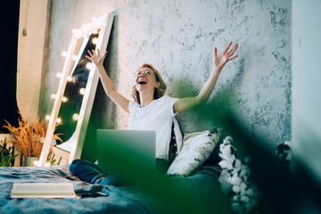 Delighted woman on bed with hands raised