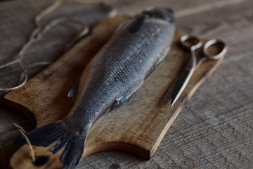 Sea bass fish on the wooden rustic table with scissors