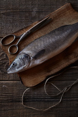 Sea bass fish on the wooden rustic table with scissors