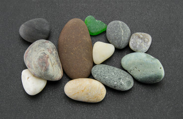A pile of smooth multi-colored stones of small size and different colors on a black textured background. Gray sea pebbles