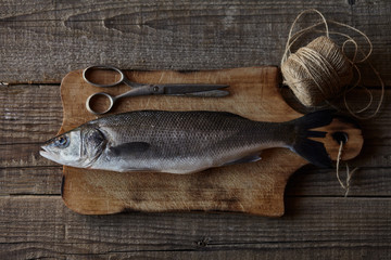 Sea bass fish on the wooden rustic table with scissors