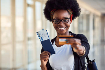 Young african american female passanger in casual clothes is in airport holding tickets and credit card