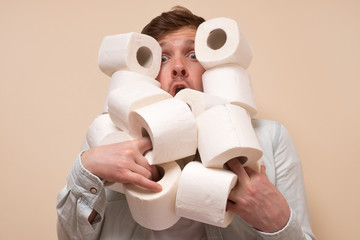 Young sad caucasian man holding several roll of toilet paper.