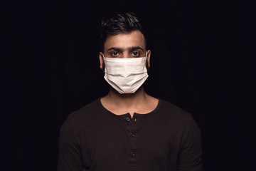 Calm man in protective mask on black background. Prevention against pneumonia, keep on being on quarantine, staying home. Chinese coronavirus treatment. Healthcare, medicine, isolation concept.
