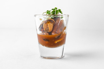 Serve a mussel appetizer in a sauce in a small glass. Beautifully decorated catering banquet menu. Food snacks and appetizers for buffet. Isolated on white background