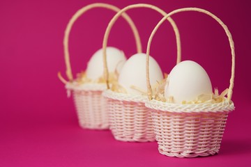 Fototapeta na wymiar White chicken eggs in a white wicker basket covered with straw a bright pink background. Holiday card with space for text.Easter symbol.Copy space.
