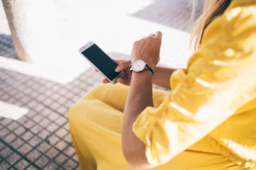 Nervous businesswoman checking time on wristwatch while using smartphone on street in city