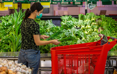 Alarmed female wears medical mask against coronavirus while grocery shopping in supermarket or store- health, safety and pandemic concept - young woman stockpiling food in fear of covid-19