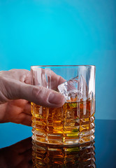 Hand taking glass with whiskey and ice on a blue background with gradient and reflection