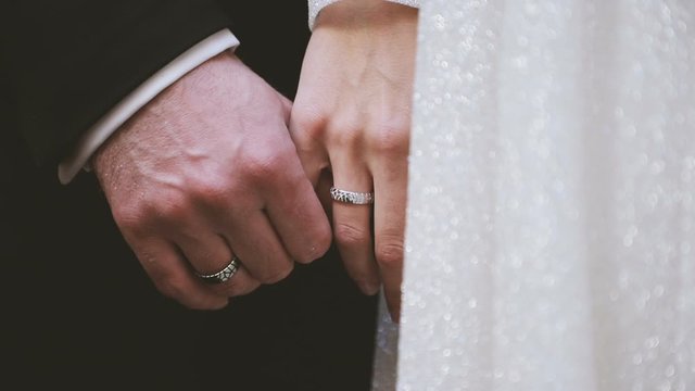 Bride and groom holding their hands with wedding rings. Close up of hands.