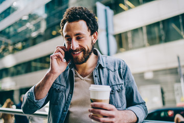 Pleased guy in casual outfit speaking on smartphone at city street