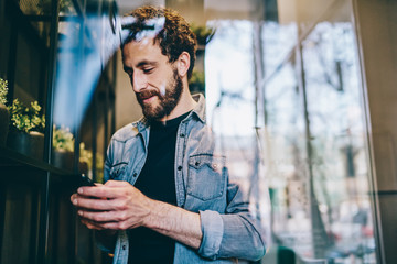 Pleased guy in casual clothing surfing on smartphone in cafe