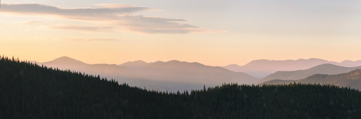 Warm gradient of dawn sky above layers of mountain and rock silhouettes. Vivid alpine landscape with dark rockies and orange sunrise sky. Minimalist highland scenery with silhouette of rocky mountains
