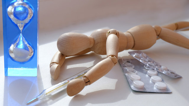 a wooden mannequin lies like a sick man, next to a thermometer and pills