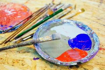 Fototapeta premium An oil paints and brushes. Close up photo. Palette with a red and blue color of paints on the wooden table.
