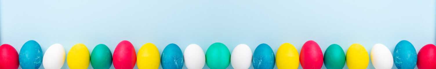 Long horizontal banner with multicolored easter eggs on blue background. Easter concept. Copy space