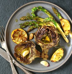 artichoke and asparagus grill. Tasty vegetables are first cooked for a couple, then fried on a grill, poured with olive oil and spices. spring vegetables.background black slate and plate as 