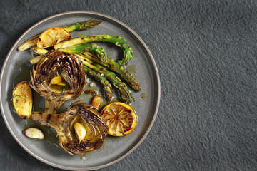 artichoke and asparagus grill. Tasty vegetables are first cooked for a couple, then fried on a grill, poured with olive oil and spices. spring vegetables.background black slate and plate as 