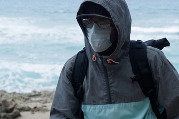 A man in sunglasses wearing a hoodie with a Medical mask on his face. oceanfront, tropical island.