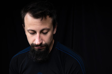 Fototapeta premium a close up portrait of a young man with beard in dark clothes on a dark background