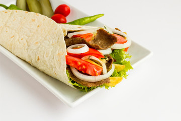 Traditional Turkish kebab "doner"wrapped with flat bread(lavas) and tomato,lettuce,onion rings and fried potatoes on long plate.Served with cucumber pickle slices,green pepper.