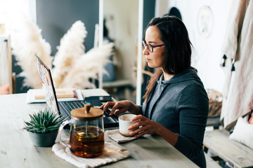 A brunette in glasses works on a laptop. Work from home or from a cozy cafe.