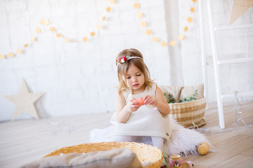 Little cute girl in a white dress plays in a bright children's room, decorated with toys and garlands.