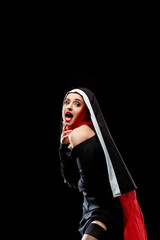 shocked sexy nun posing in black dress, stockings and red scarf, isolated on black