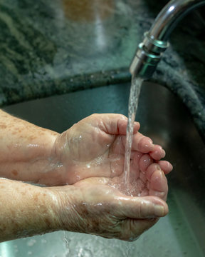 M&atilde;os de uma idoso sendo lavada com &aacute;gua corrente  