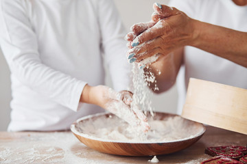 Close up view of woman with her granddaughter preparing food with flour on kitchen