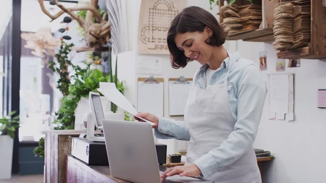 Female owner of florists shop working on laptop behind sales desk - shot in slow motion